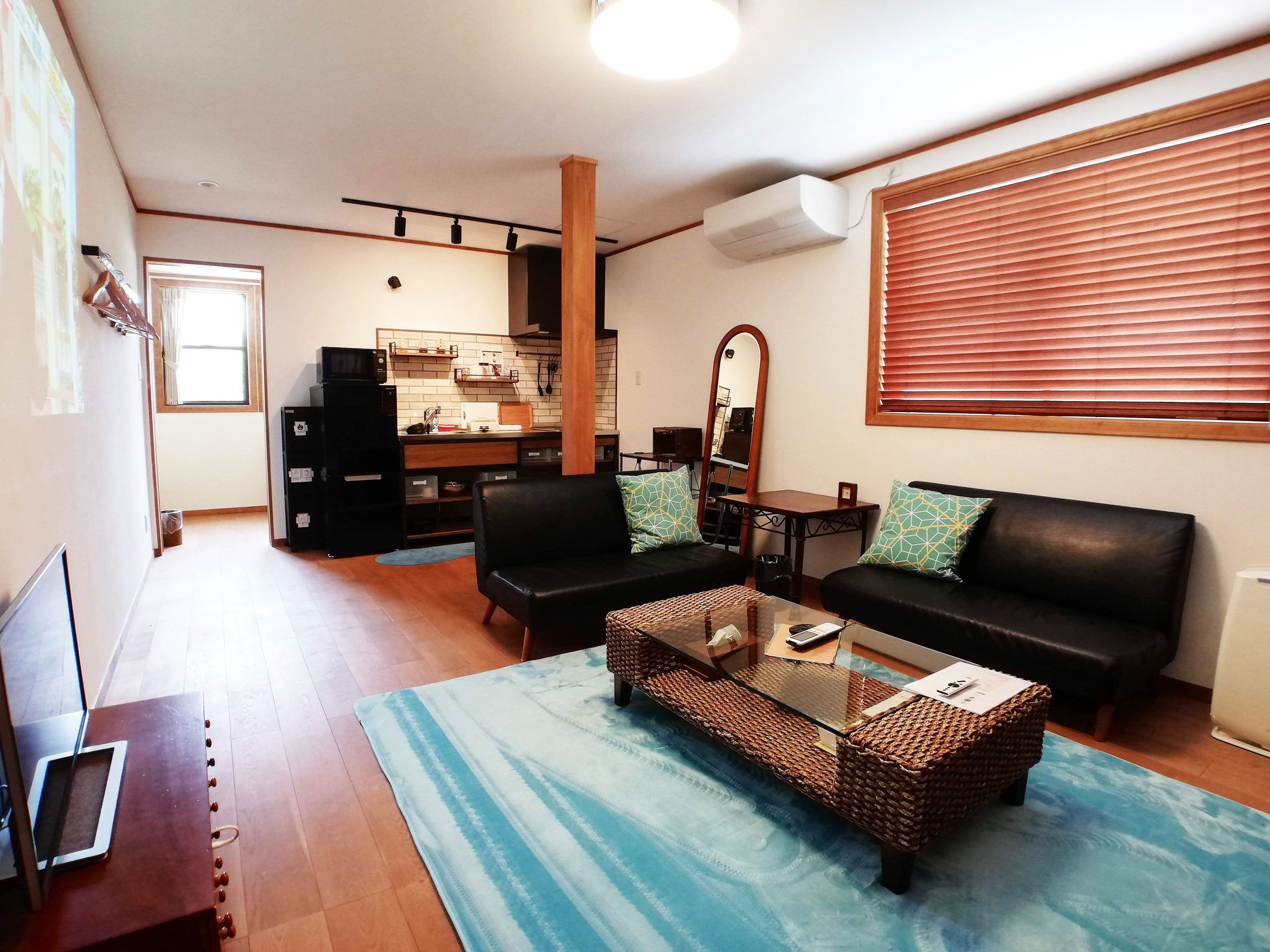 広々とした客室。漆喰の壁と床の無垢材が事前を感じさせる。キッチンと青いじゅうたんが特徴的なお部屋